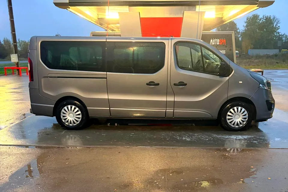 Pilkas Opel Vivaro mikroautobusas iš šono prie plovyklos, šlapias asfaltas